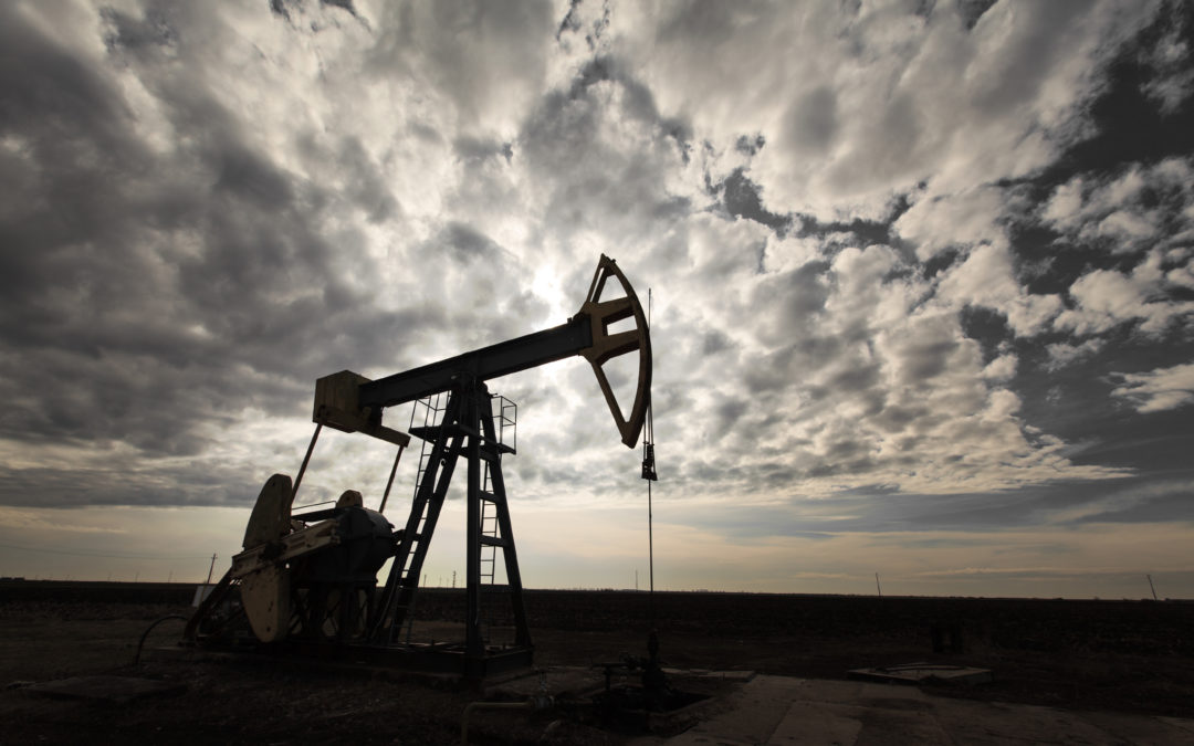 an oil rig on a large field against a vast and wide cloudy sky